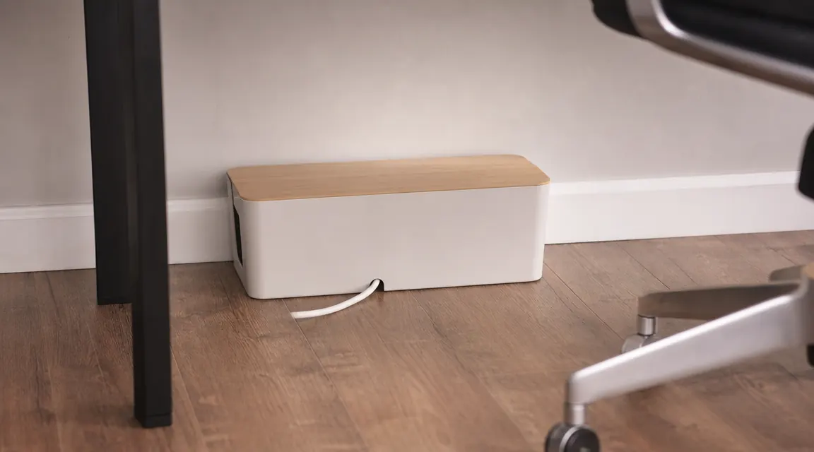 Cable box sitting on the floor beside a desk with a single power strip cord visible running into it